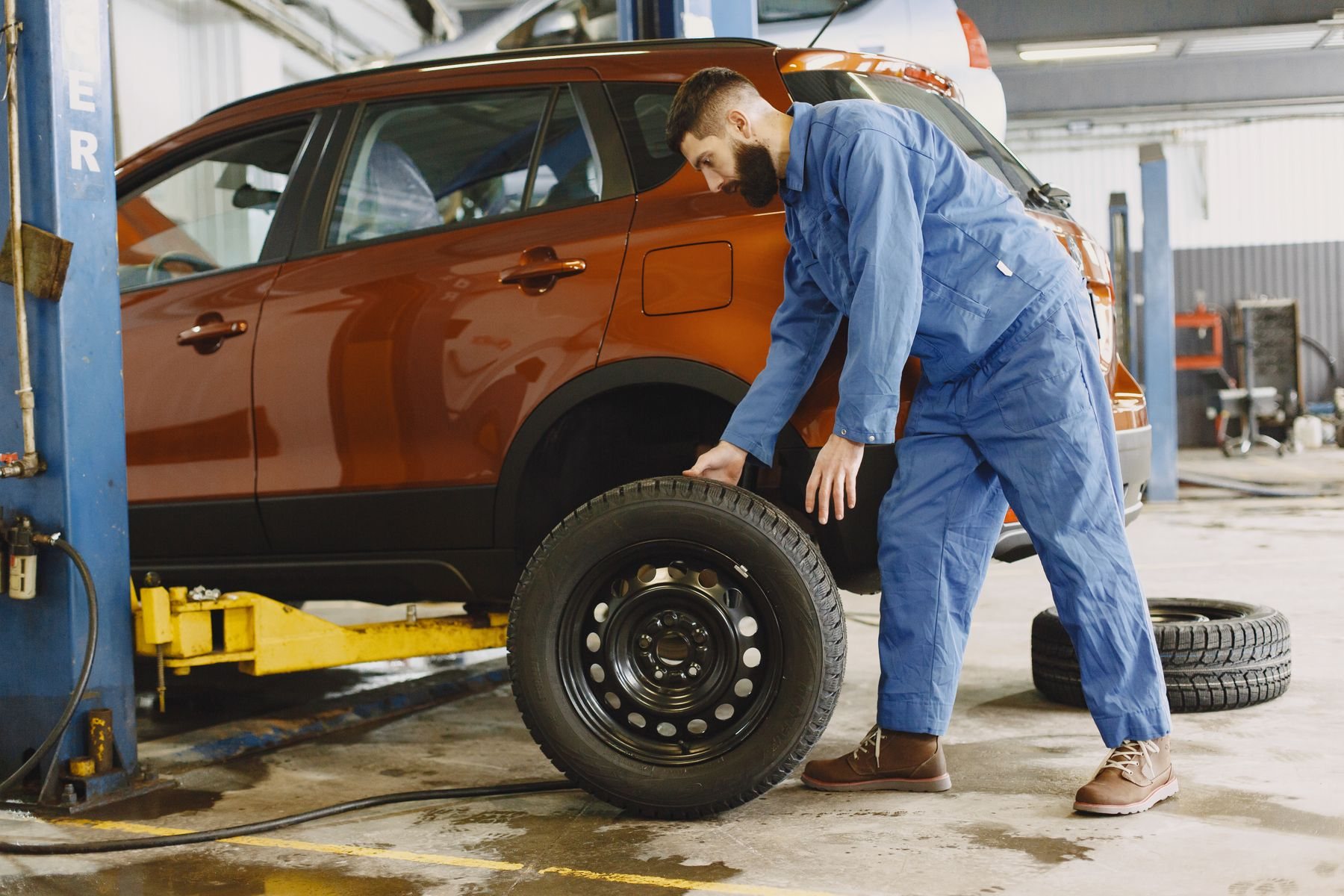 Technician rolling a steel wheel beside a two-post lift holding a crossover, yellow lift arms visible