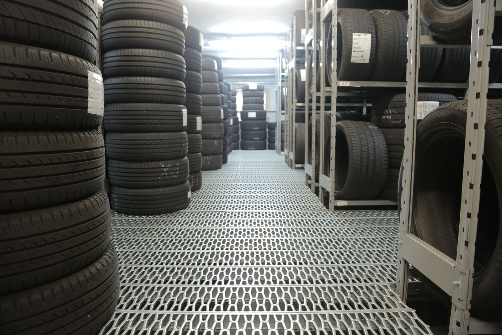 Stacks of new passenger and light-truck tires on steel racks in a working shop warehouse